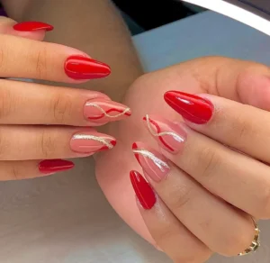 Unhas decoradas com esmalte vermelho e detalhes dourados, seguindo tendências de 2025.