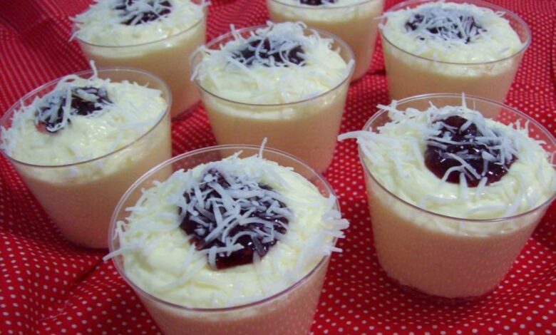 Mousses de coco cremosos servidos em copinhos, decorados com coco ralado e geleia de frutas vermelhas.