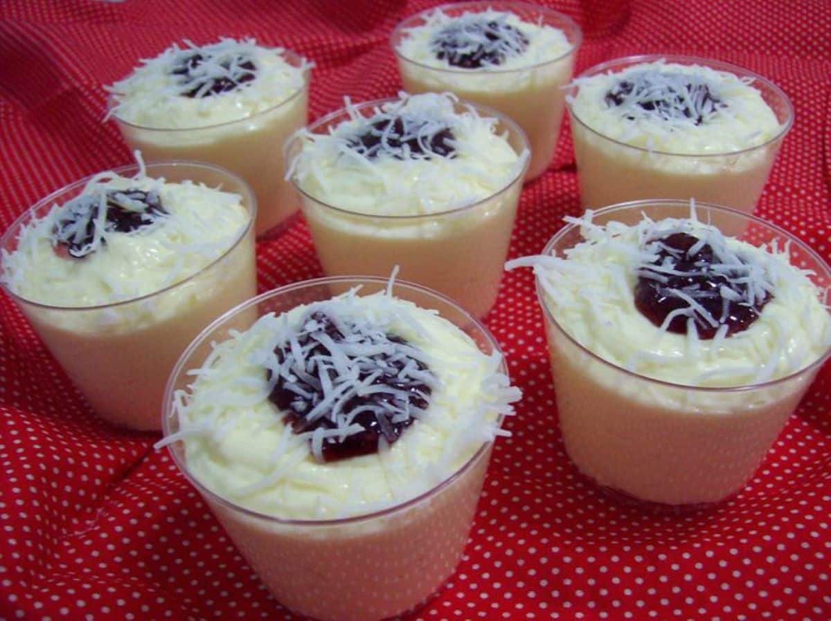 Mousses de coco cremosos servidos em copinhos, decorados com coco ralado e geleia de frutas vermelhas.