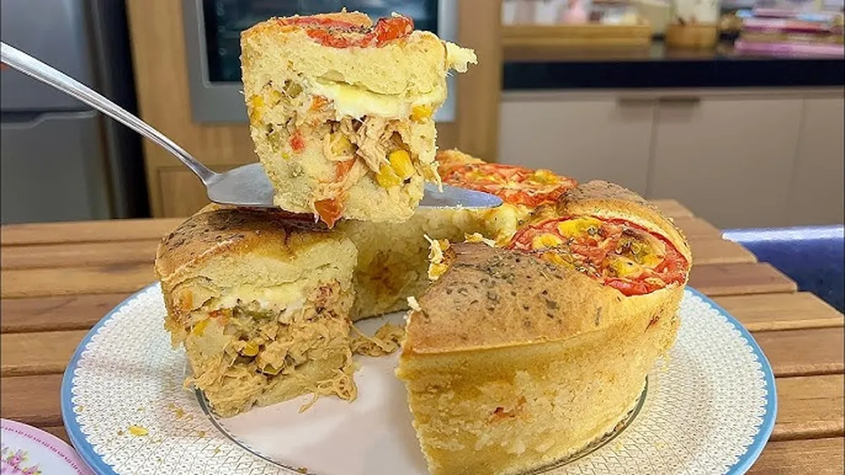 Torta salgada recheada com frango, milho e queijo, com uma fatia sendo servida.