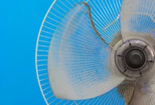 Ventilador com pás sujas de poeira contra um fundo azul.