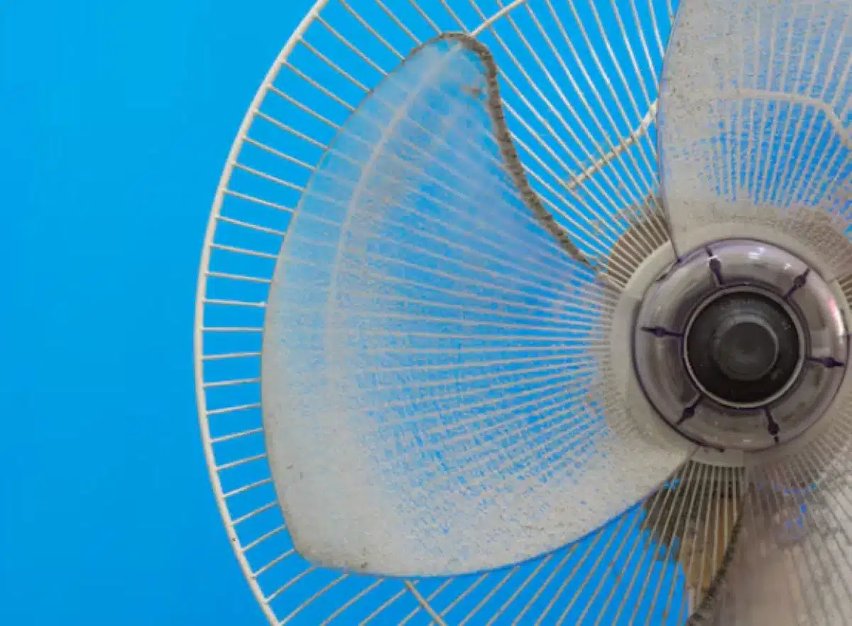 Ventilador com pás sujas de poeira contra um fundo azul.