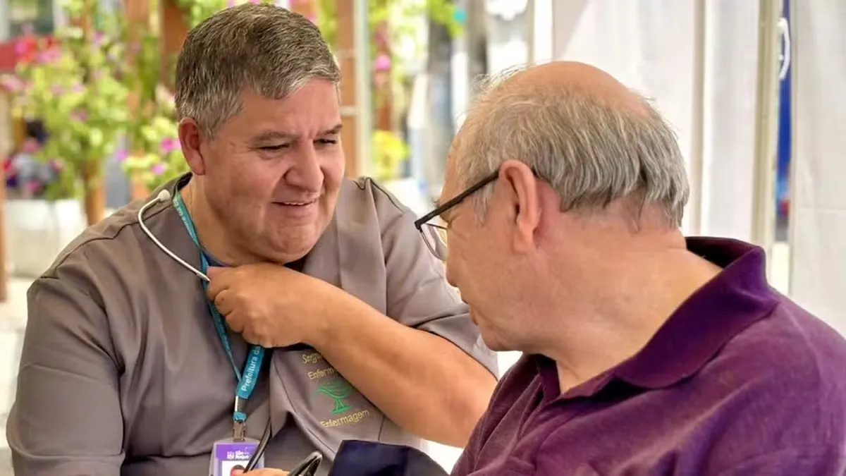 Enfermeiro sorridente atende idoso durante ação de saúde comunitária.