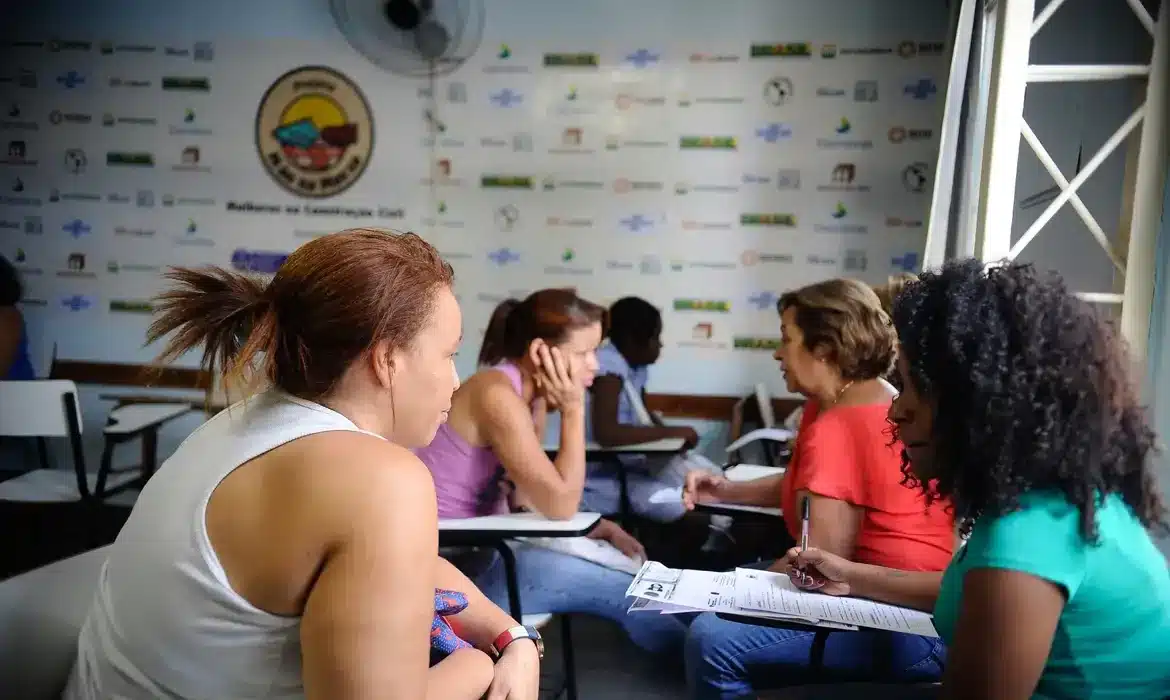 Grupo de pessoas sentadas em uma sala, discutindo documentos, possivelmente para regularização de benefícios.