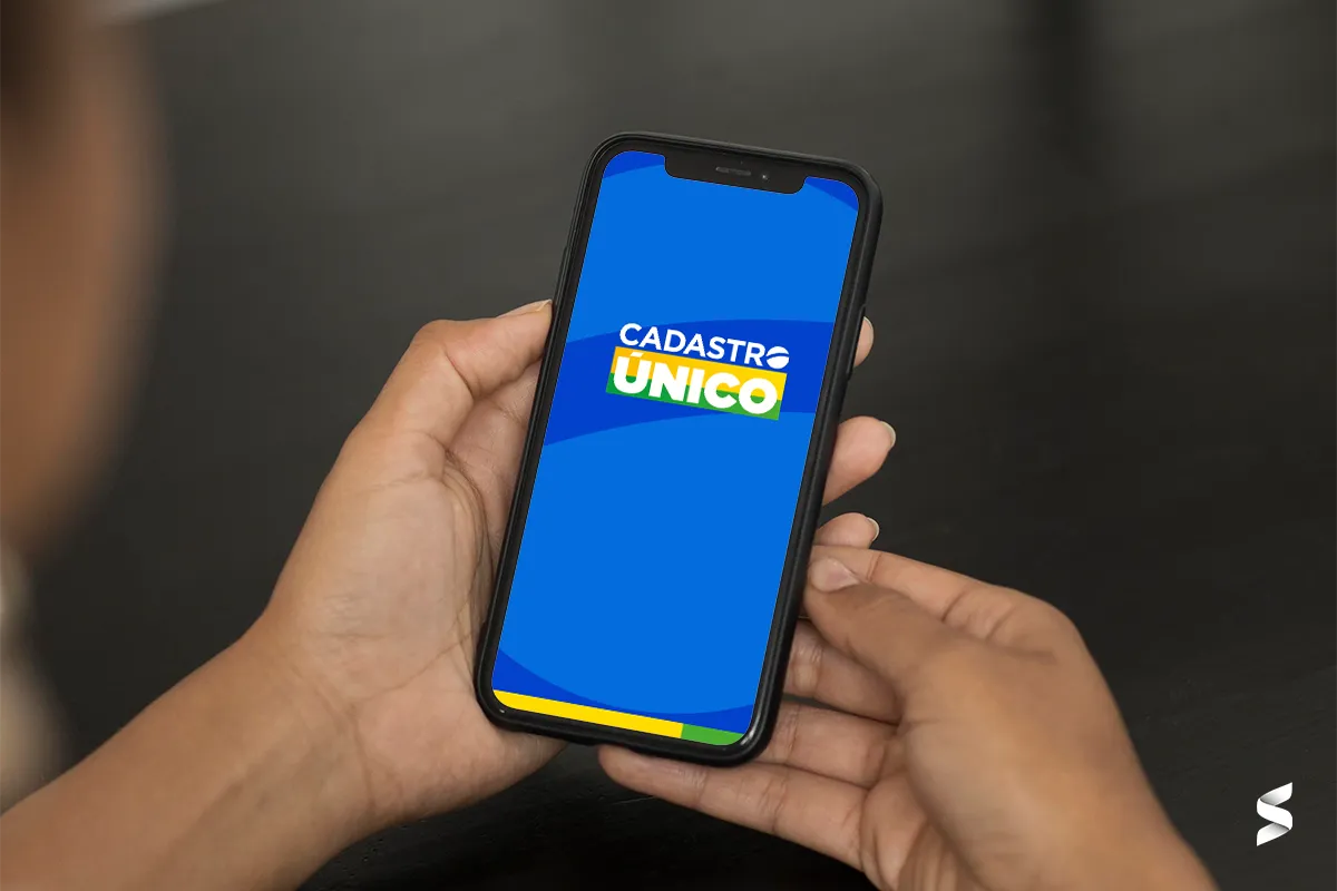 Mão segurando um celular com o logo do Cadastro Único na tela, ilustrando o processo de consulta ao CadÚnico.