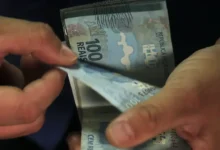 Mãos contando cédulas de 100 reais, representando pagamento de benefícios.