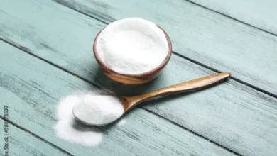 Bicarbonato de sódio em uma tigela de madeira e uma colher de madeira, com fundo de madeira clara.