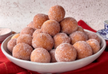 Bolinho de chuva de fubá empilhado, com açúcar por cima, em um prato branco, em fundo neutro.