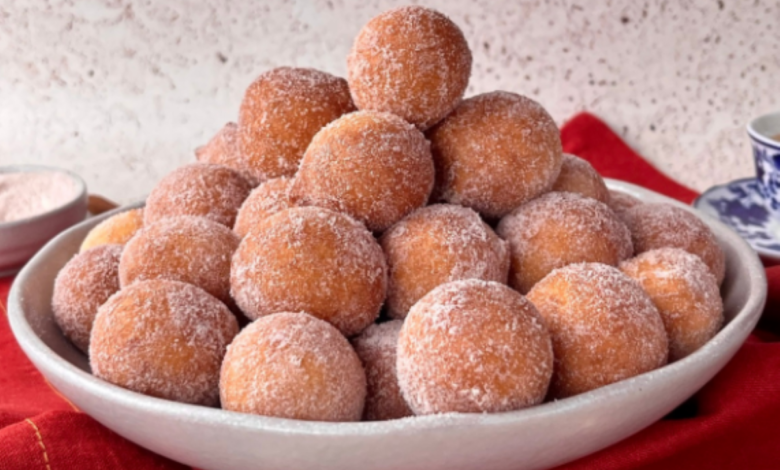 Bolinho de chuva de fubá empilhado, com açúcar por cima, em um prato branco, em fundo neutro.