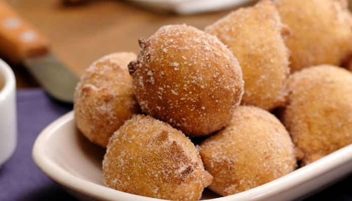 Bolinho de chuva de fubá, dourado e coberto com açúcar cristal, servido em uma travessa branca.