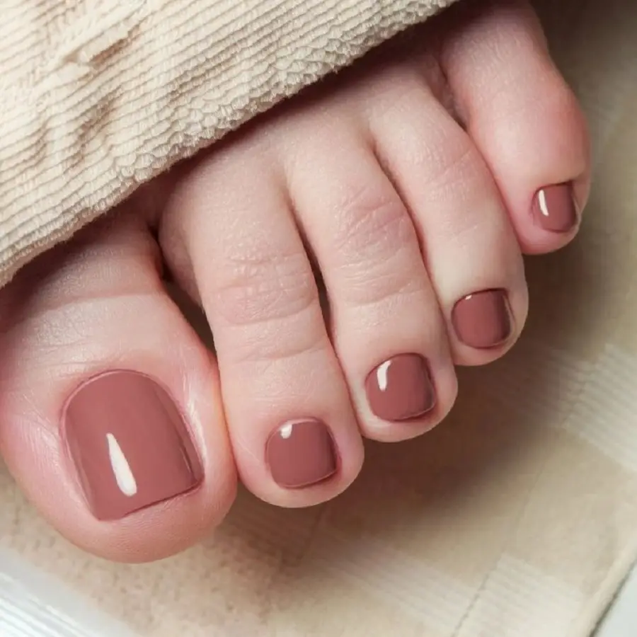 Unhas dos pés pintadas com esmalte nude terroso, transmitindo naturalidade e sofisticação