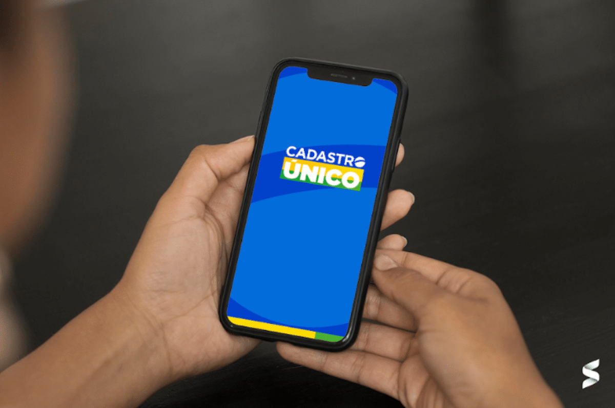 Pessoa segura celular exibindo a tela inicial do aplicativo Cadastro Único (CadÚnico), relacionado ao tema de visitas do governo em 2025.