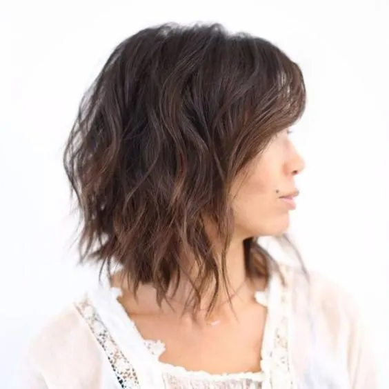 Mulher com corte choppy bob em camadas sutis, cabelos ondulados castanhos e estilo leve.