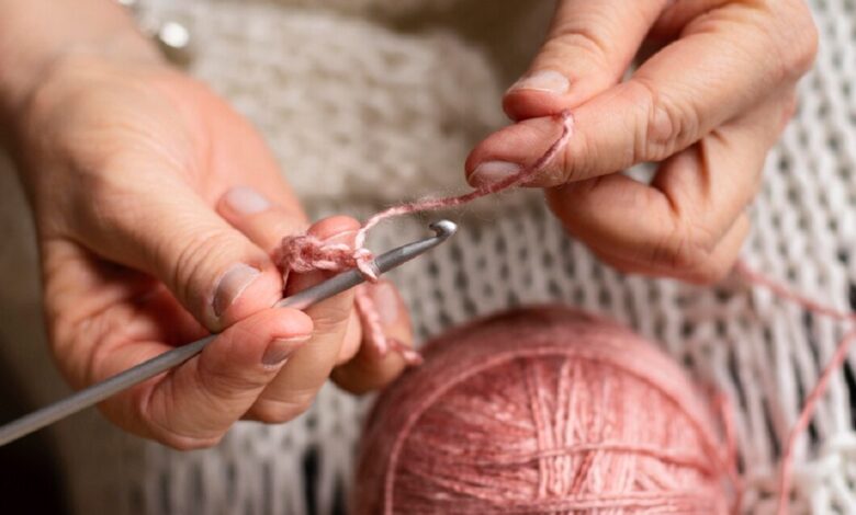 Mãos segurando agulha de crochê e linha rosa, iniciando um novo projeto artesanal.