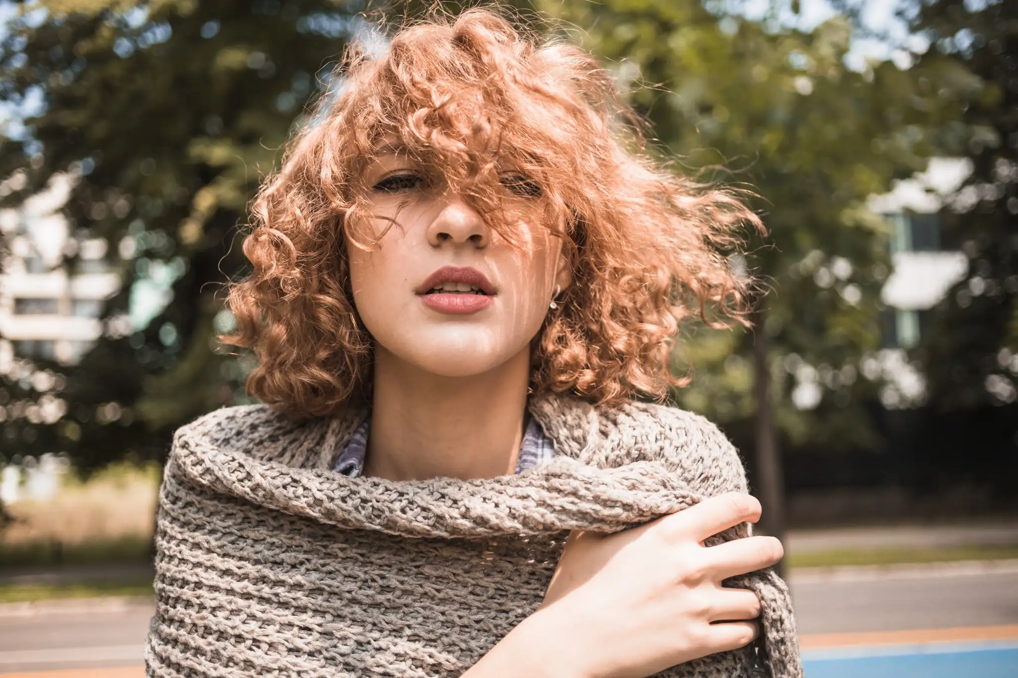 Mulher com cabelo cacheado volumoso ao ar livre, vestindo um cachecol de tricô.