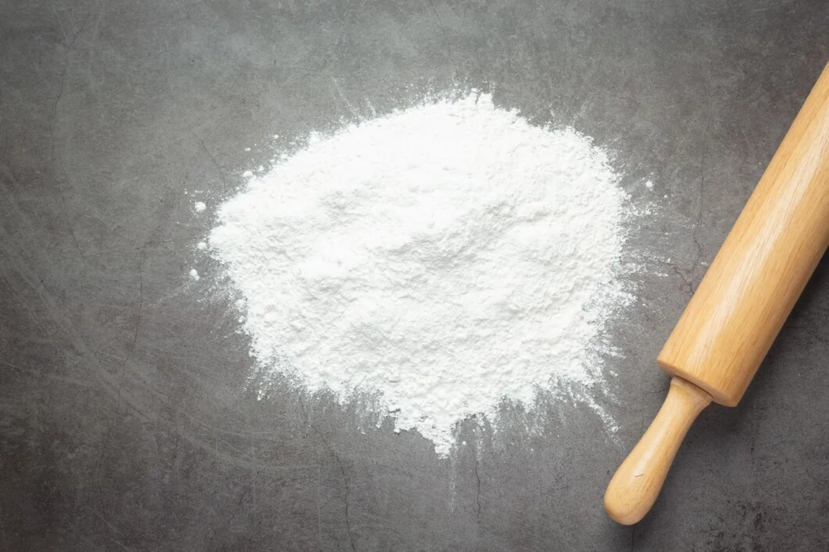 Imagem de farinha e utensílios de cozinha, representando a preparação de alimentos que utilizam bicarbonato de sódio ou fermento em pó.