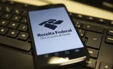 Celular exibindo o logotipo da Receita Federal sobre um teclado de computador.