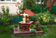 Jardim com decoração rústica, poço decorativo de madeira e vasos de plantas ao redor.