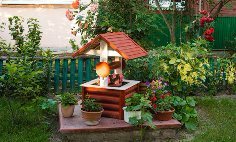 Jardim com decoração rústica, poço decorativo de madeira e vasos de plantas ao redor.