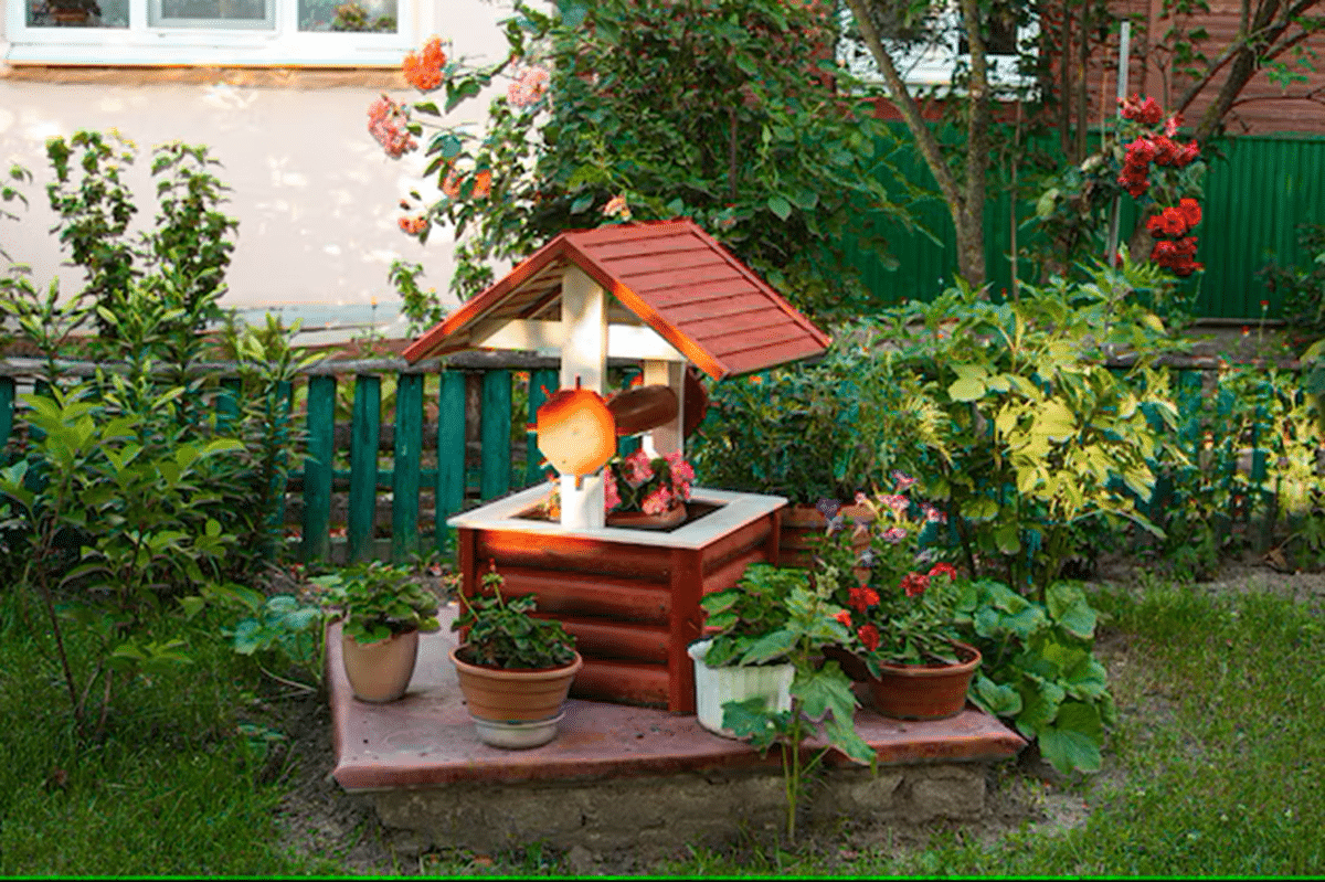Jardim com decoração rústica, poço decorativo de madeira e vasos de plantas ao redor.