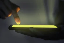 Mão interagindo com a tela de um smartphone iluminado no escuro