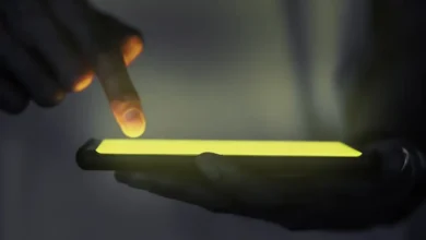 Mão interagindo com a tela de um smartphone iluminado no escuro