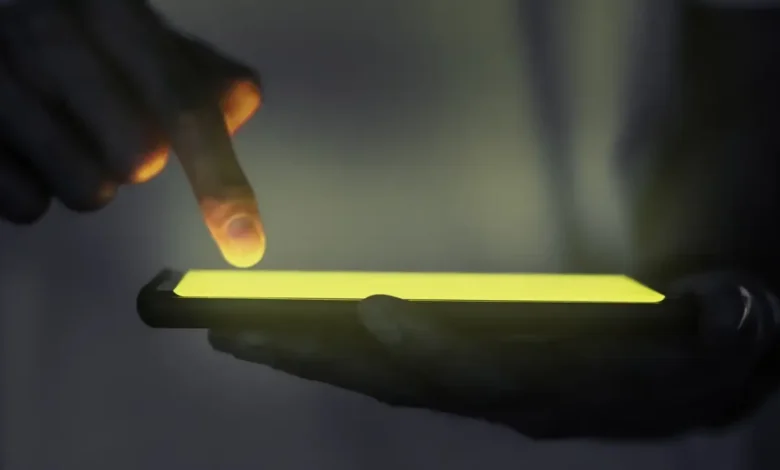 Mão interagindo com a tela de um smartphone iluminado no escuro