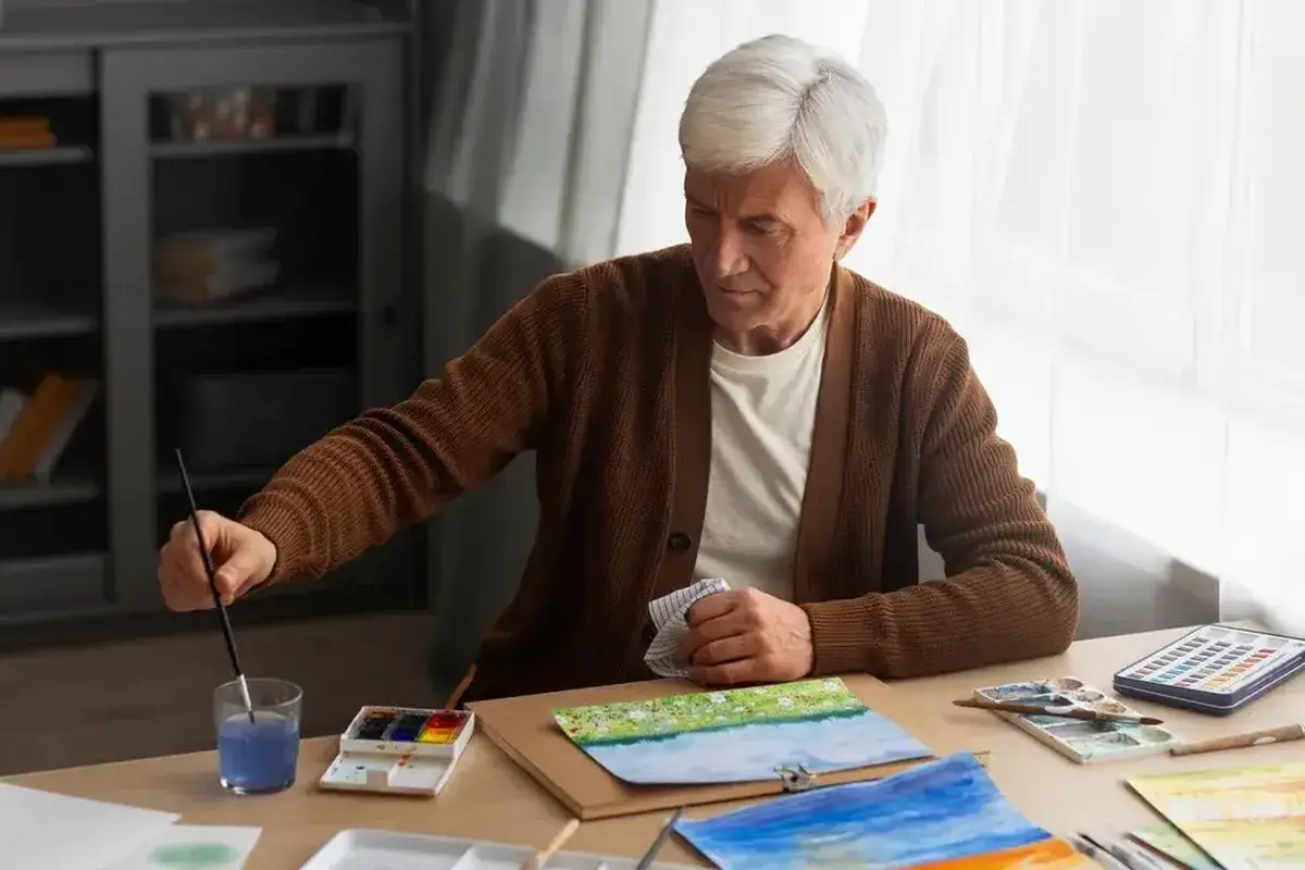 Idoso praticando arteterapia com pintura em aquarela em um ambiente iluminado.