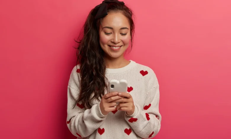 Jovem sorrindo enquanto digita mensagens fofas de boa noite em seu celular.