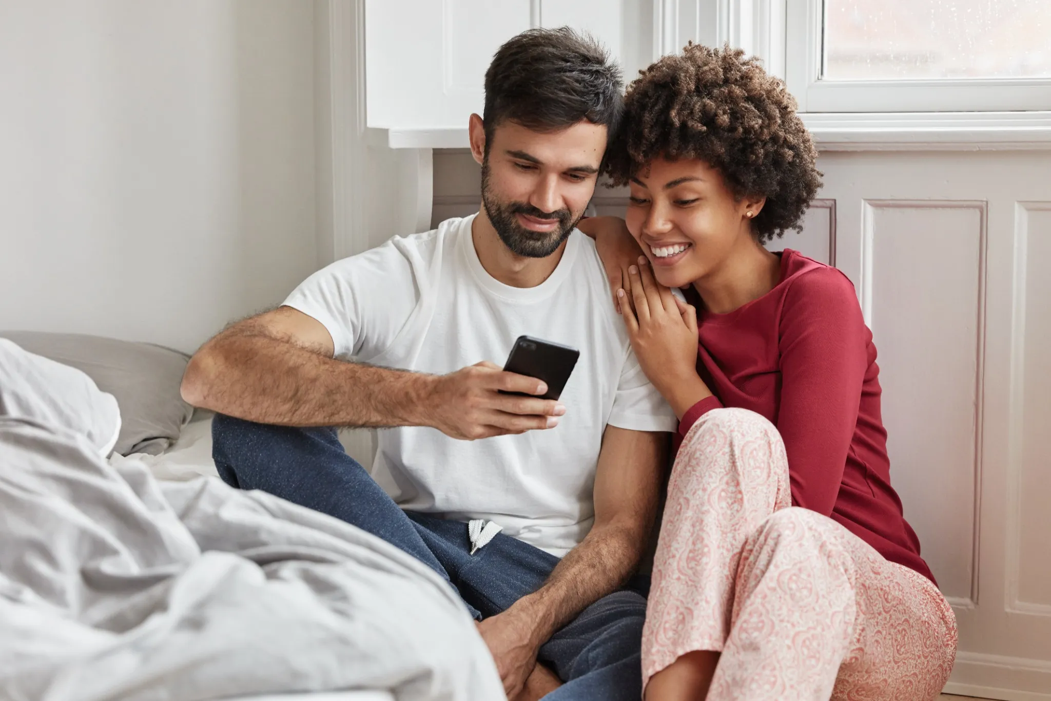 Casal sorrindo enquanto compartilham uma mensagem fofa de boa noite em seu celular.