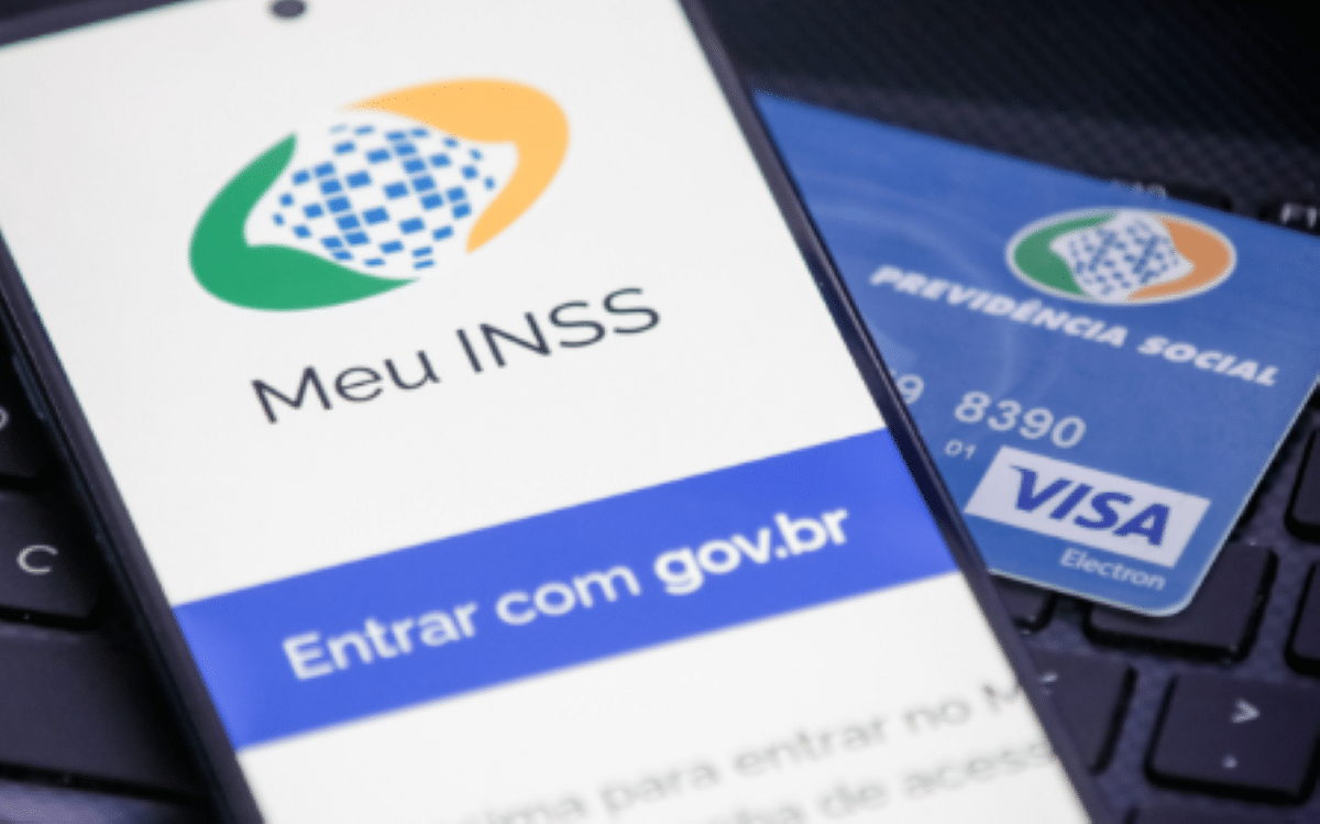 Aplicativo Meu INSS aberto ao lado de cartão da Previdência Social e teclado, representando acesso digital a benefícios do INSS.