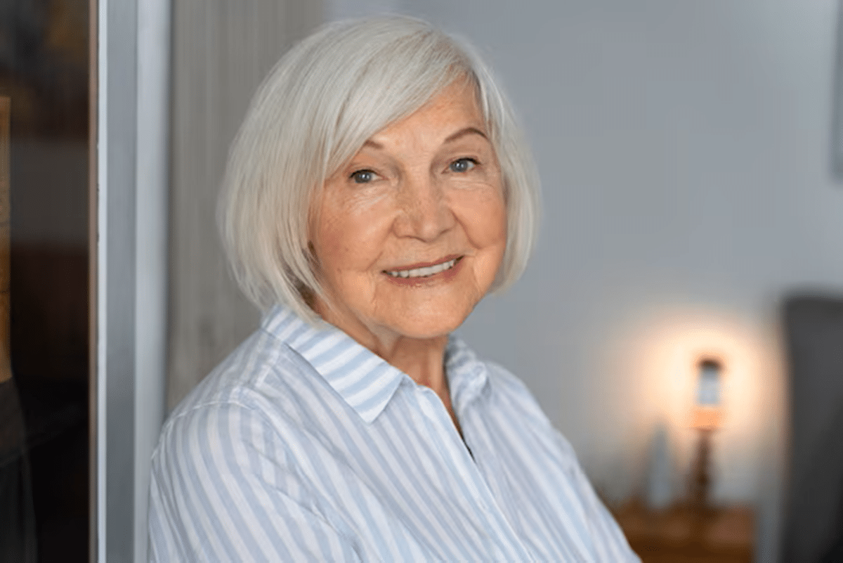 Mulher idosa de cabelos grisalhos sorrindo e vestindo uma camisa listrada.