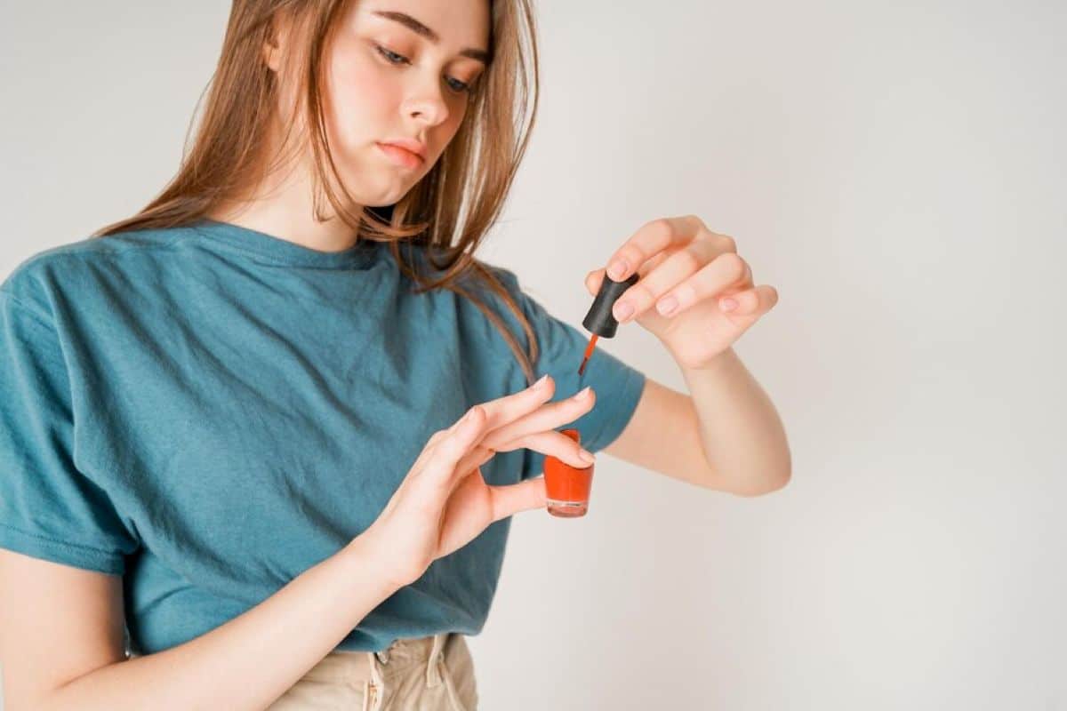 Mulher aplicando esmalte vermelho nas unhas, representando o cuidado com a beleza e elegância.