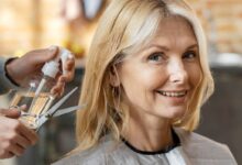 Mulher madura sorridente no salão de beleza enquanto cabeleireiro prepara corte.