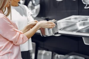 Duas mulheres analisam uma panela de alumínio em uma loja de utensílios de cozinha.