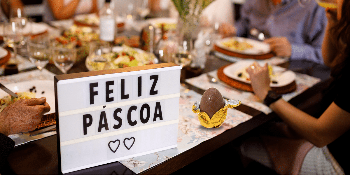 Mesa de jantar com decoração de Páscoa, incluindo um ovo de chocolate e uma mensagem "Feliz Páscoa", simbolizando o feriado.