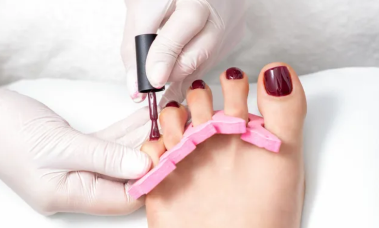 Imagem de uma pedicure sendo feita em um pé com esmalte roxo escuro, representando tendências de cores de esmalte para os pés em 2025.