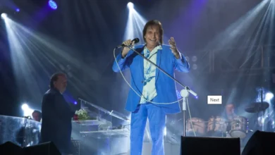 Roberto Carlos se apresentando no palco em um show, vestindo um terno azul e segurando um microfone