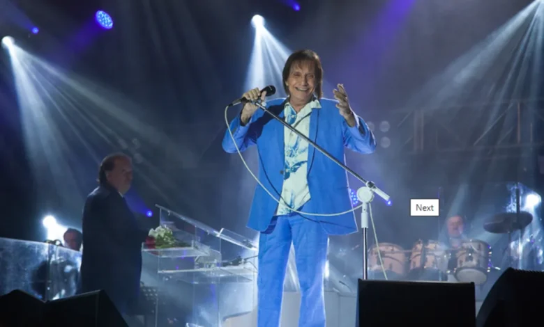 Roberto Carlos se apresentando no palco em um show, vestindo um terno azul e segurando um microfone