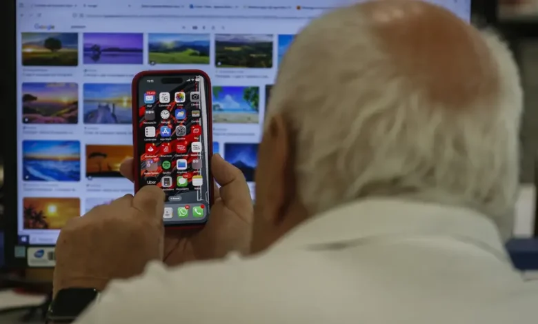 Idoso segurando um iPhone com diversos aplicativos na tela, incluindo o WhatsApp.