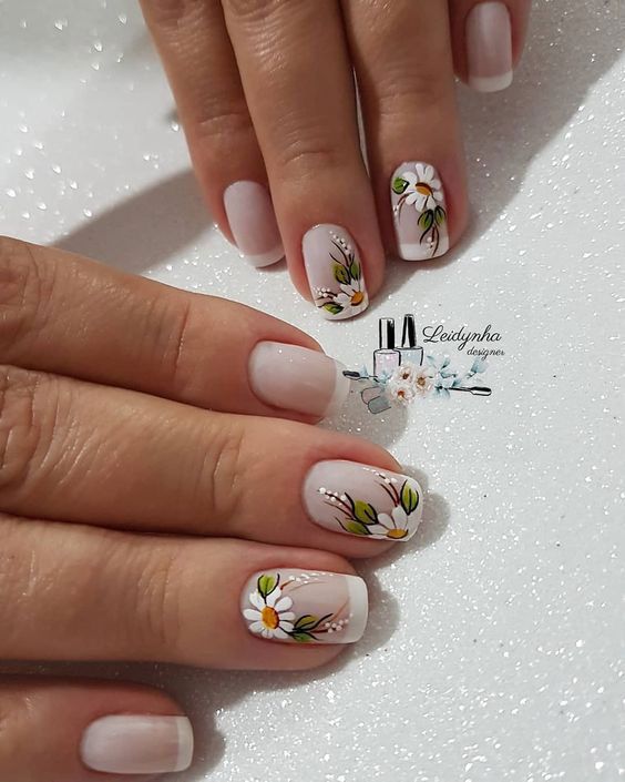 Unhas com design floral delicado, fundo nude e flores pintadas em tons de branco e verde