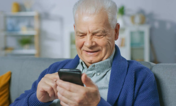 Idoso sentado no sofá utilizando um smartphone com expressão de satisfação