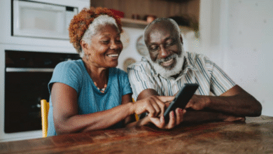 Casal de idosos sorrindo enquanto usa um smartphone juntos na cozinha
