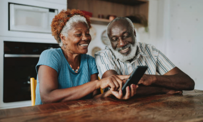 Casal de idosos sorrindo enquanto usa um smartphone juntos na cozinha