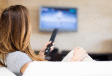 Pessoa assistindo à televisão, provavelmente assistindo uma novela turca, com controle remoto nas mãos.