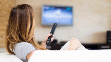 Pessoa assistindo à televisão, provavelmente assistindo uma novela turca, com controle remoto nas mãos.