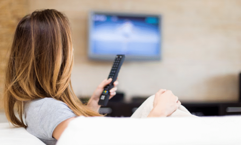 Pessoa assistindo à televisão, provavelmente assistindo uma novela turca, com controle remoto nas mãos.