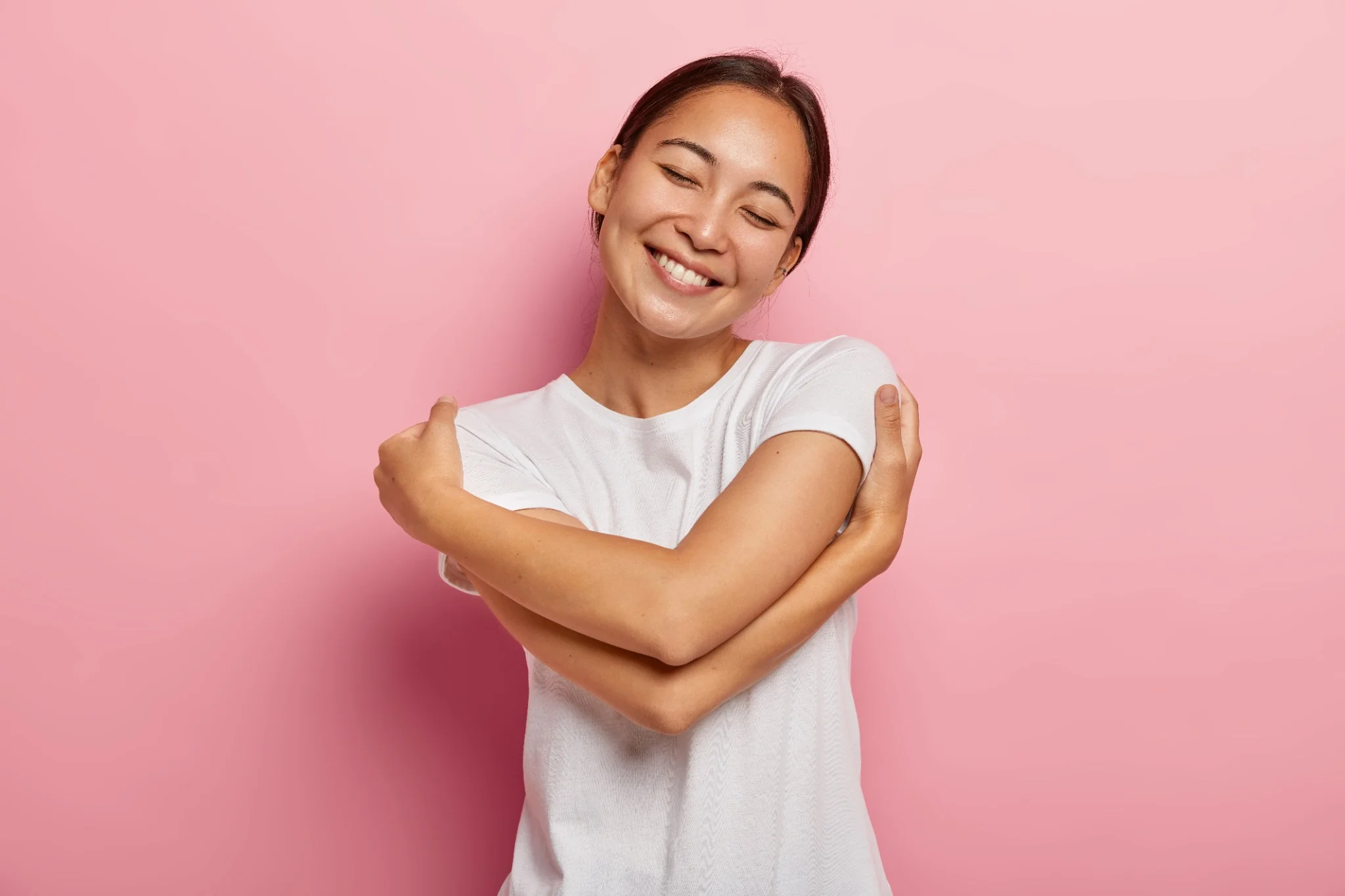 Mulher sorrindo e se abraçando, transmitindo a ideia de autocuidado e amor próprio.