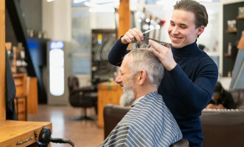 Homem maduro sorrindo enquanto corta o cabelo em estilo low fade em barbearia moderna.