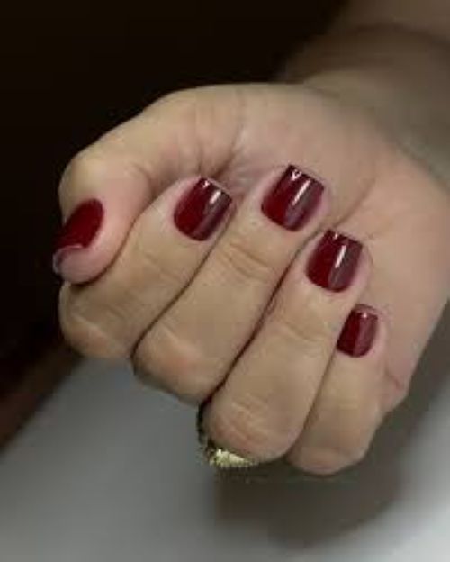 Unhas pintadas com esmalte vermelho escuro, mostrando um acabamento impecável em uma mão feminina.